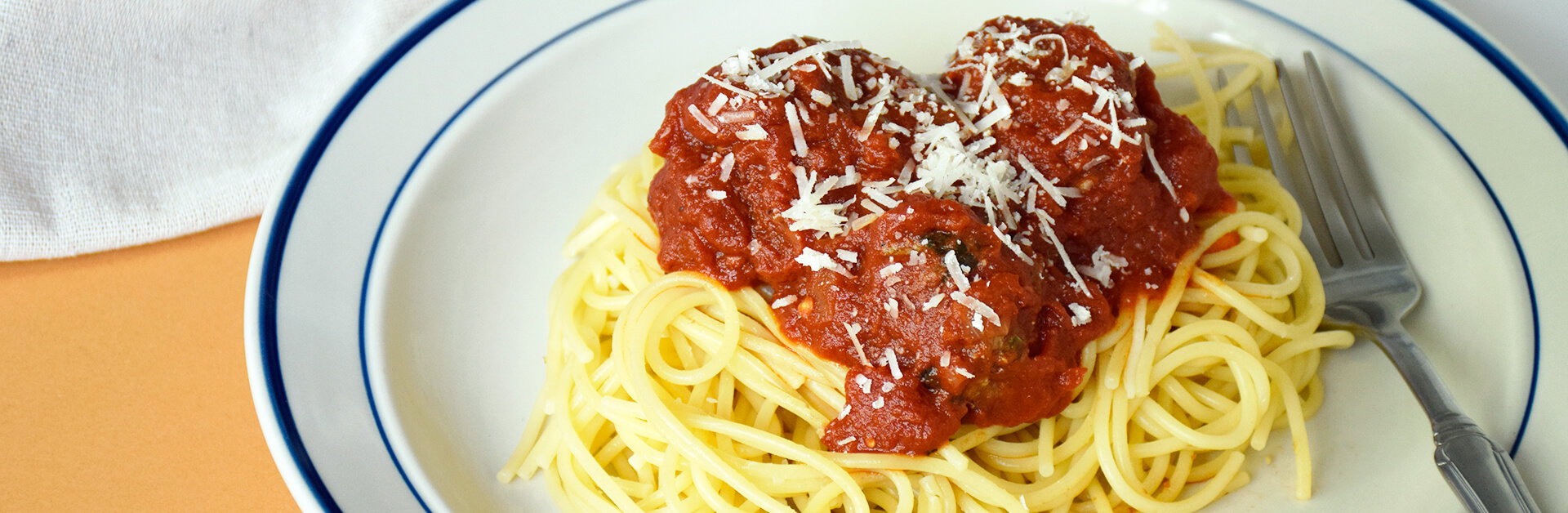 Spaghetti and meatballs on a white plate with blue edges.